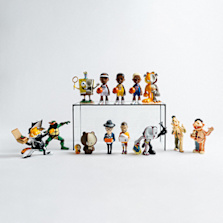 "Various colorful figurines of cartoon and pop culture characters, including SpongeBob, basketball players, Garfield, and other toys, arranged on and in front of a clear rectangular stand against a white background."