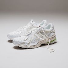 A pair of New Balance 1906 sneakers in all-white with subtle green accents, displayed on a clean, minimal surface.