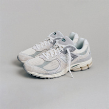 A pair of New Balance 1906 sneakers in all-white with subtle green accents, displayed on a clean, minimal surface.