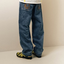 Person wearing loose-fitting blue jeans with embroidered back pockets, standing indoors with yellow and black sneakers."