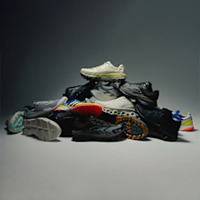 "A pile of various performance running shoes arranged in a pyramid shape on a neutral background, showcasing different colors, soles, and designs."