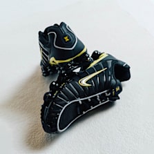 Two black Nike Shox sneakers with yellow accents stacked on a white background.