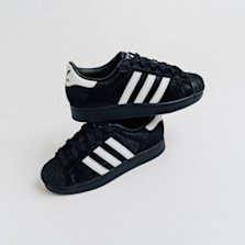 Adidas Superstar sneakers in black with white stripes and black shell toes, styled in a cross-stacked position on a clean white background.