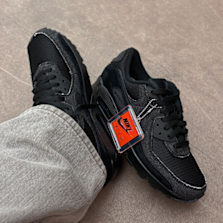 Nike Air Max 90 “Black Denim” sneakers in an all-black denim construction, worn with light grey trousers, highlighting the textured upper and iconic Air Max cushioning.