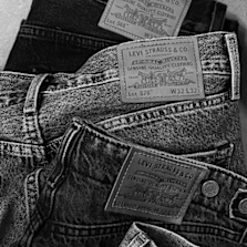 Stack of Levi’s jeans in black and washed grey denim, showcasing signature leather patches and classic five-pocket construction against a textured denim background.  Geben Sie Ihr Feedback zu BizChat ab.