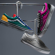 Three Vans Pearlized sneakers featuring pearl-inspired studs and metallic accents, suspended from chrome rails against a grey background. The styles include a white pair, a pink-and-black pair, and a multicolored pair with green, blue, and yellow panels.