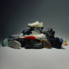 "A pile of various performance running shoes arranged in a pyramid shape on a neutral background, showcasing different colors, soles, and designs."