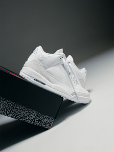 A single white Air Jordan 3 sneaker with elephant print detailing, placed on top of its black and grey patterned shoebox.