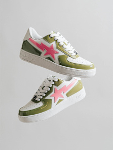 Two BAPE STA sneakers, one above the other, featuring white, olive green patent leather, and a prominent pink star logo, against a light grey background.