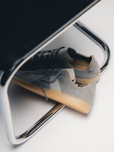 Close-up of adidas BW Army Decon sneakers in grey suede with a translucent gum sole, placed on a chrome chair against a clean, minimal background.