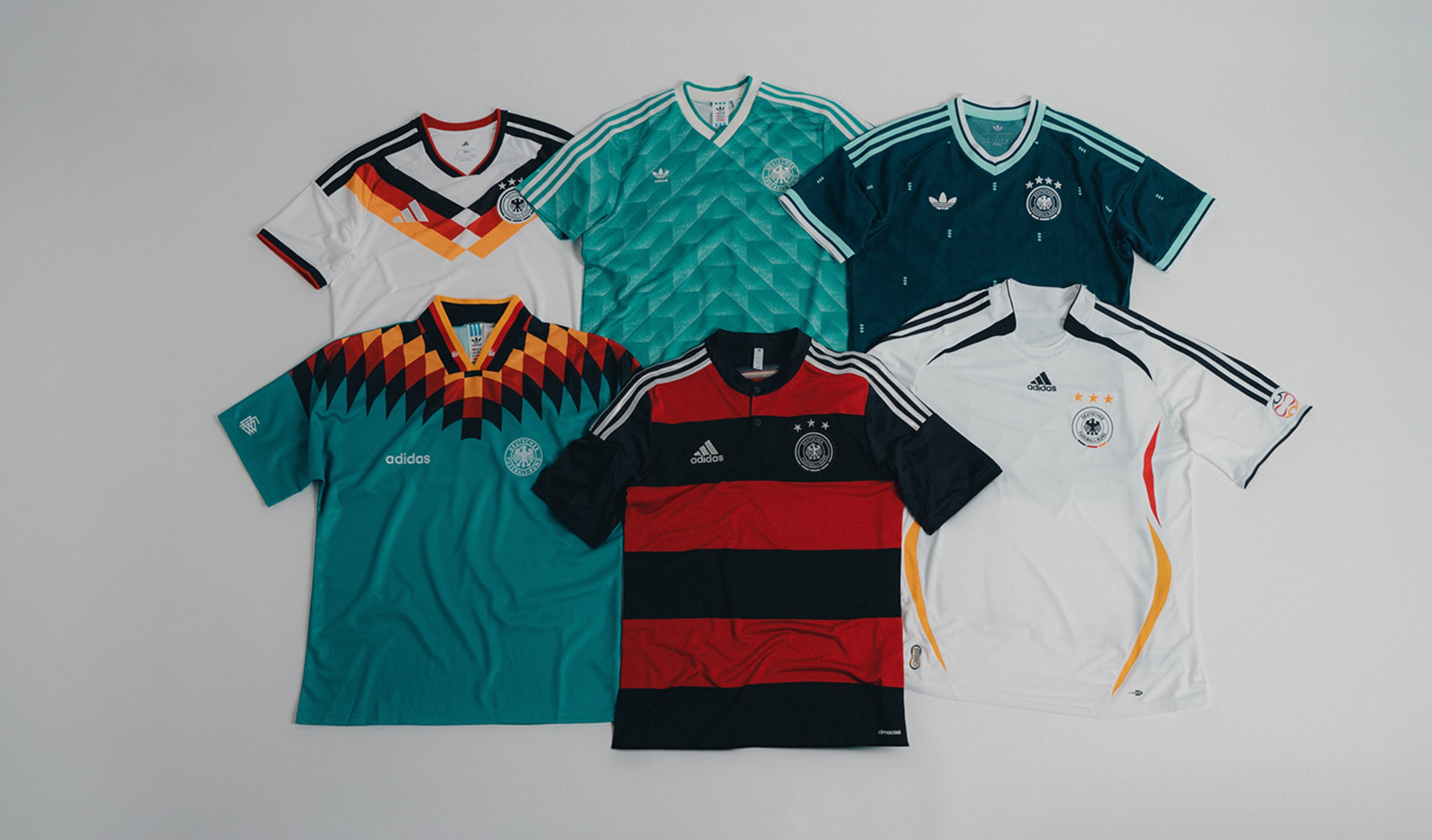 Six adidas DFB Germany jerseys laid flat on a light background, showcasing different designs and colors including white, green, teal, black, and retro-inspired patterns, each featuring the Germany crest and adidas branding.