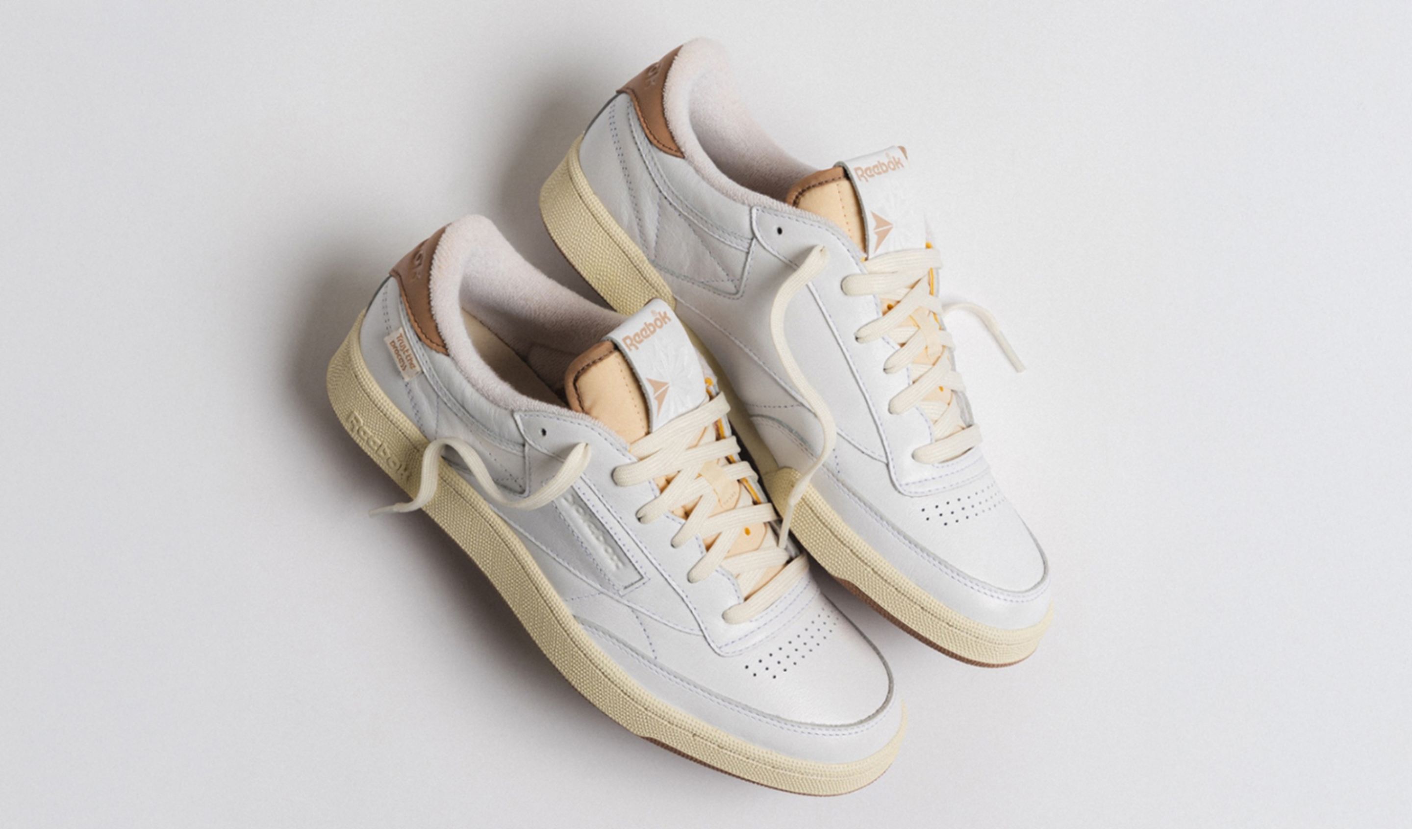 White Reebok sneakers with beige details, one shoe standing upright showing the sole with Reebok logo.