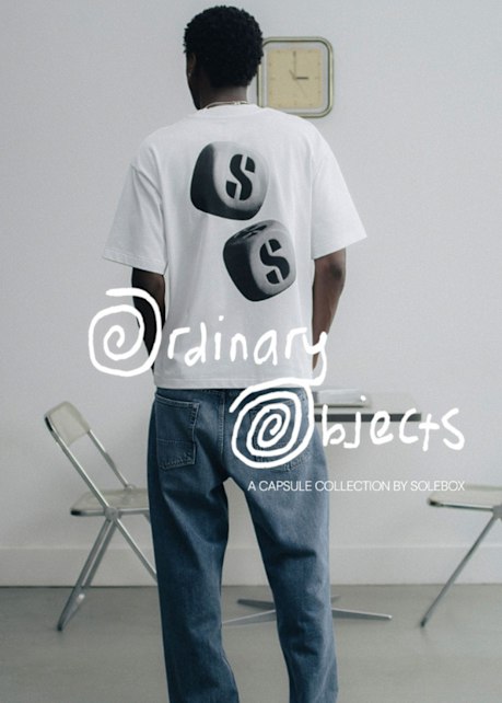 Person wearing a white solebox Ordinary Objects T-shirt with a black dice graphic on the back, paired with blue jeans in a minimalist interior setting.