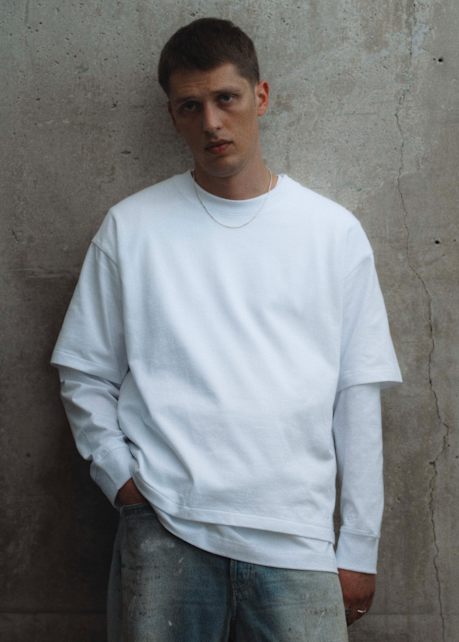 Person wearing a white layered top and light-wash jeans from the solebox Core Collection, standing against a concrete wall.