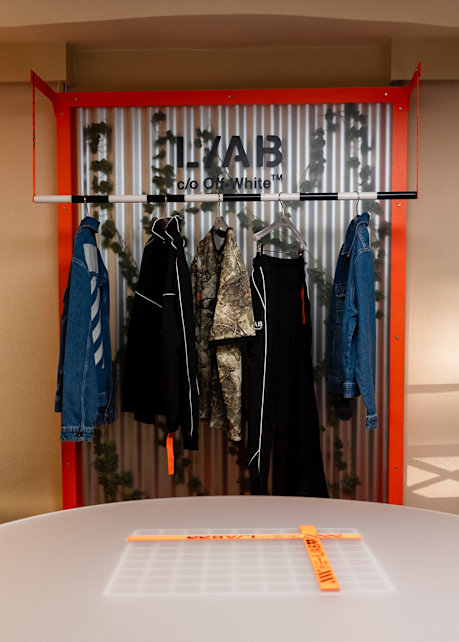 Display from the LAB c/o Off-White™ collection, featuring denim, outerwear, and technical apparel on a clothing rack within a branded showroom installation.