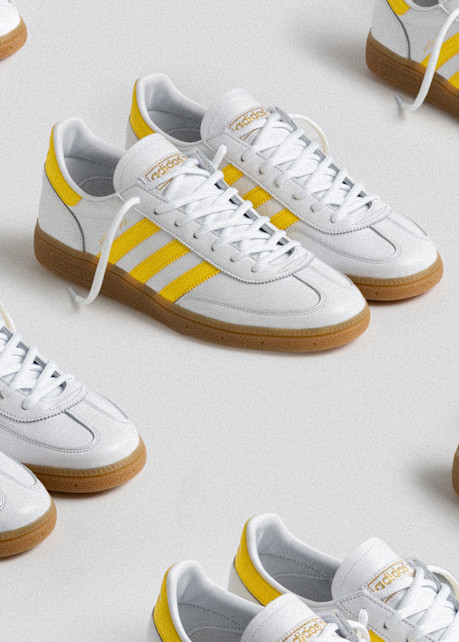 Multiple pairs of adidas x Solebox Handball Spezial sneakers in white leather with yellow three stripes and gum soles on a light background.