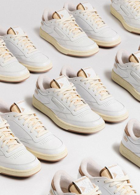 Multiple pairs of white Reebok sneakers with beige accents arranged in a repeating pattern on a light surface.